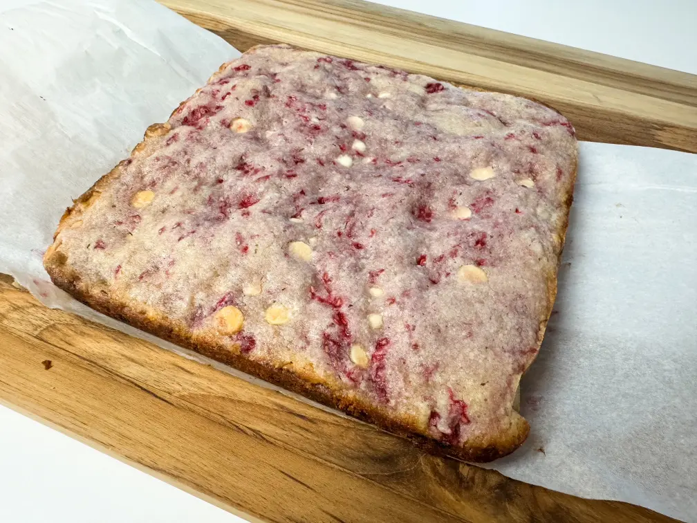 Baked raspberry white chocolate blonde brownies on a wooden board.