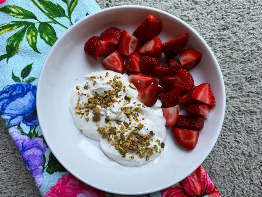 bowl of whipped greek yogurt with pistachios and a side of strawberries.